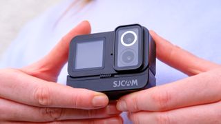 A photo of the SJCAM Sj20 being held in a person's hands with the lenses showing against a blue backdrop.