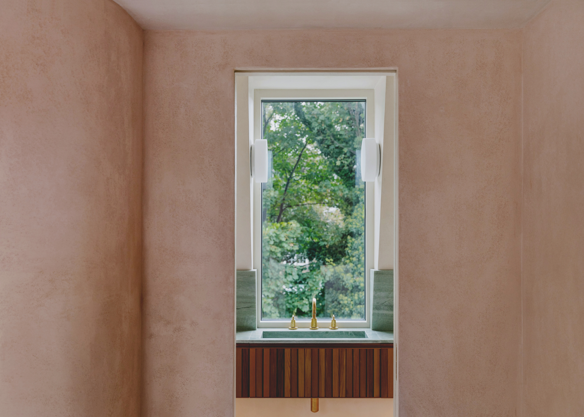 shot into an ensuite bathroom with a window above the green marble sink with wooden cabinetry beneath