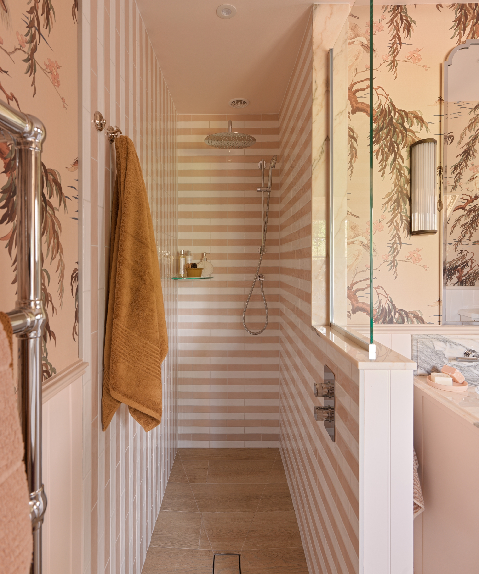 A shower room with horizontal white and pink striped tiles, silver hardware, and a botanical wallpaper