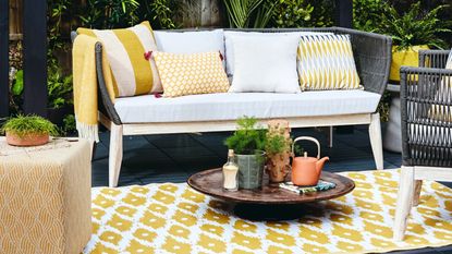 Outdoor sofa with colourful cushions on a stone path with a firepit