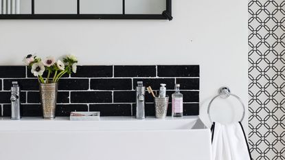 Black and white bathroom, modern basin, lattice window mirror,. black tiled splashback, black wall light, hand towel