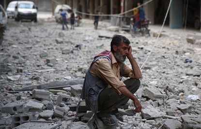 A man kneels in rubble in Douma, Syria.