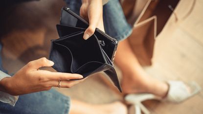 A woman, only her hands and legs showing, opens her empty wallet.