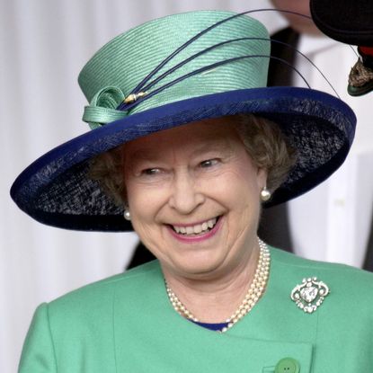 Queen Elizabeth wears a green jacket with a green and navy hat and laughs