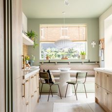 a pale green and beige kitchen with wooden cabinetry and banquette seating around a round dining table