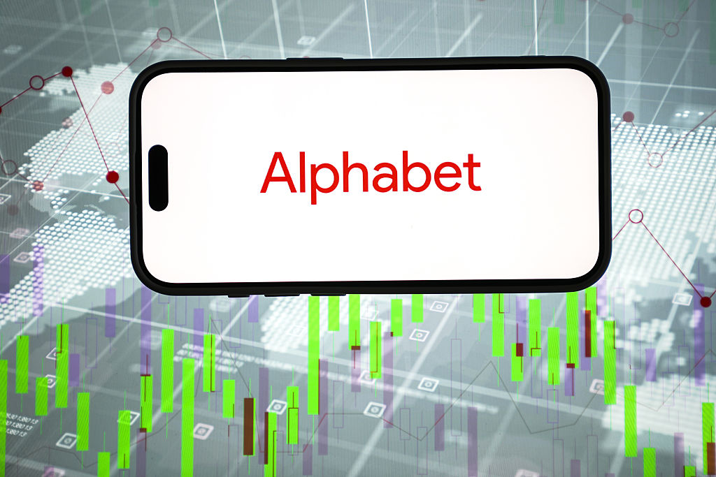 Alphabet logo is displayed on a mobile phone screen with share price charts in the background