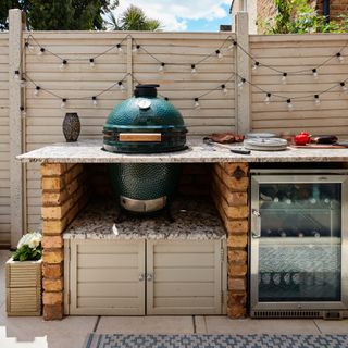outdoor kitchen with bricks and marble cooking area, outdoor fridge, festoon lights, rug