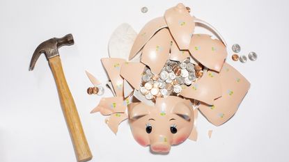 A hammer sits next to a shattered piggy bank filled with coins.