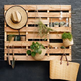 Black painted brick exterior wall with wall-mounted pallet used as garden storage