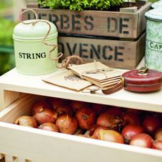 Harvested onions in wooden drawer below string tin, seed packets, tape measure and wooden crate for herbs