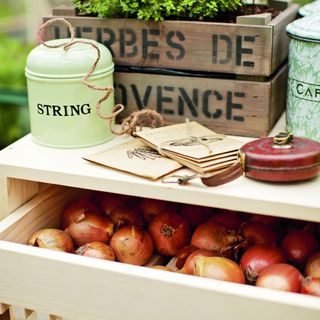 Harvested onions in wooden drawer below string tin, seed packets, tape measure and wooden crate for herbs