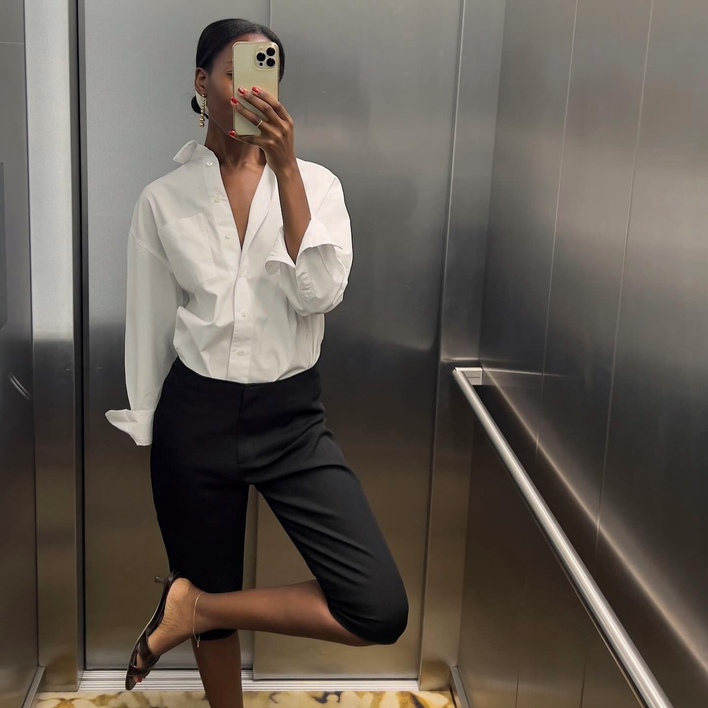 French woman wears black capri pants, white button down and black sandals in a mirror selfie. 