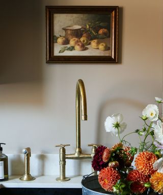 A kitchen sink with flowers inside and a painting hanging above