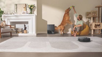 Lifestyle image of the eufy X10 Pro Omni cleaning carpet while a man plays with his dog next to the self-emptying station