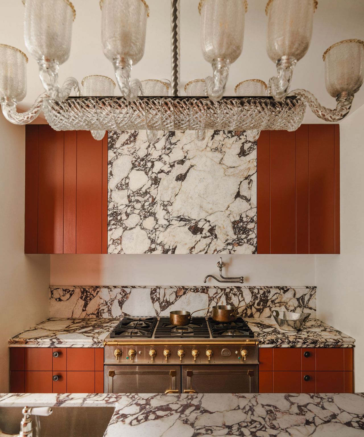 Kitchen with marble worktops and rust coloured cabinets and vintage style glass pendant light