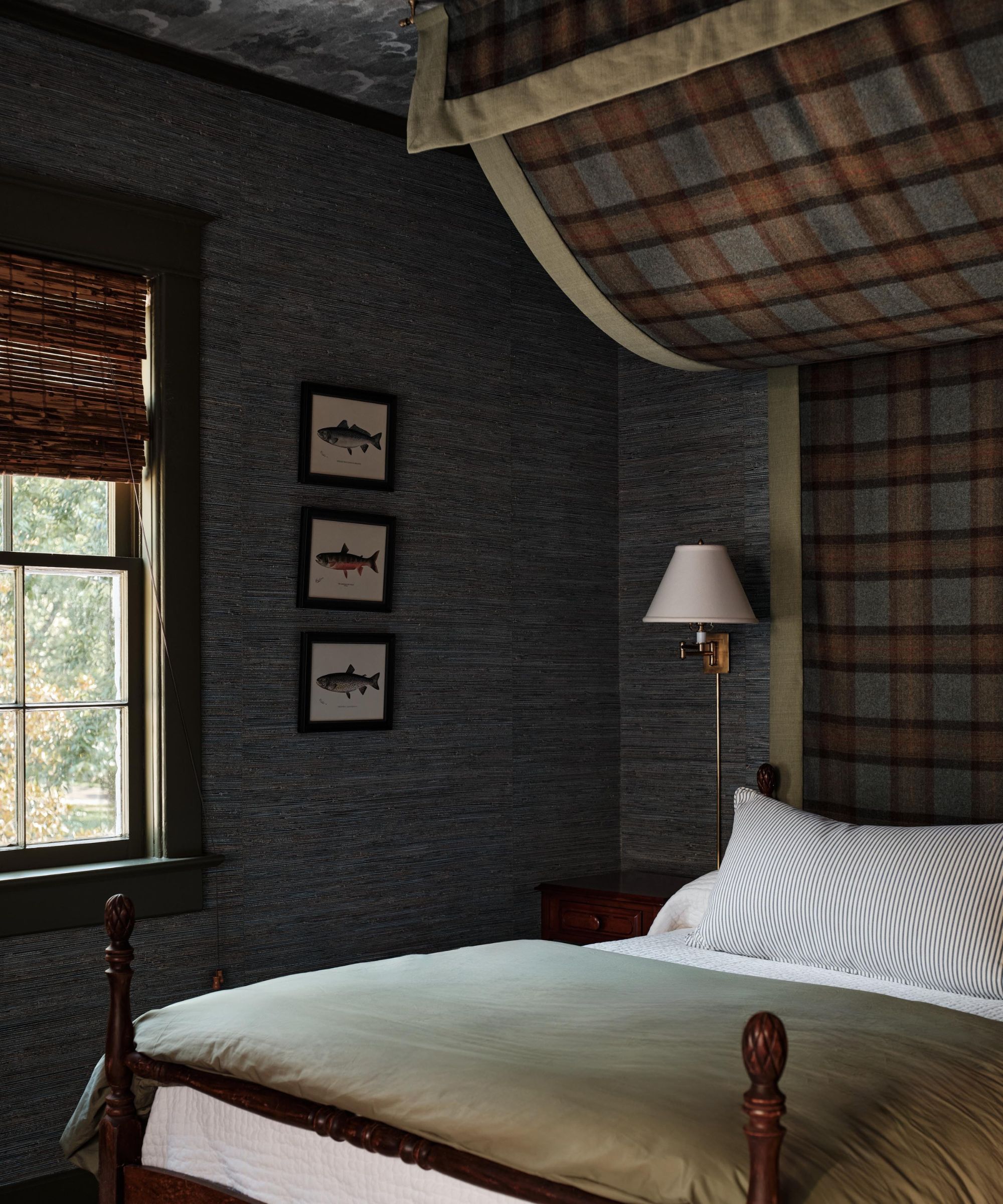 a cozy, mountain-inspired bedroom with seagrass walls, fish wall art, a bed with a striped pillow and green bedding, and a plaid cover hanging above the bed