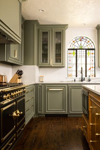 Green Shaker-style kitchen with black range cooker and dark wood floorboards