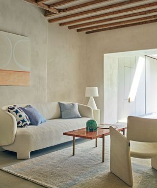 minimalist beige living room with sofa, armchair and limewash walls