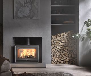 A log burning stove in agrey living room with logs stacked in an alcove