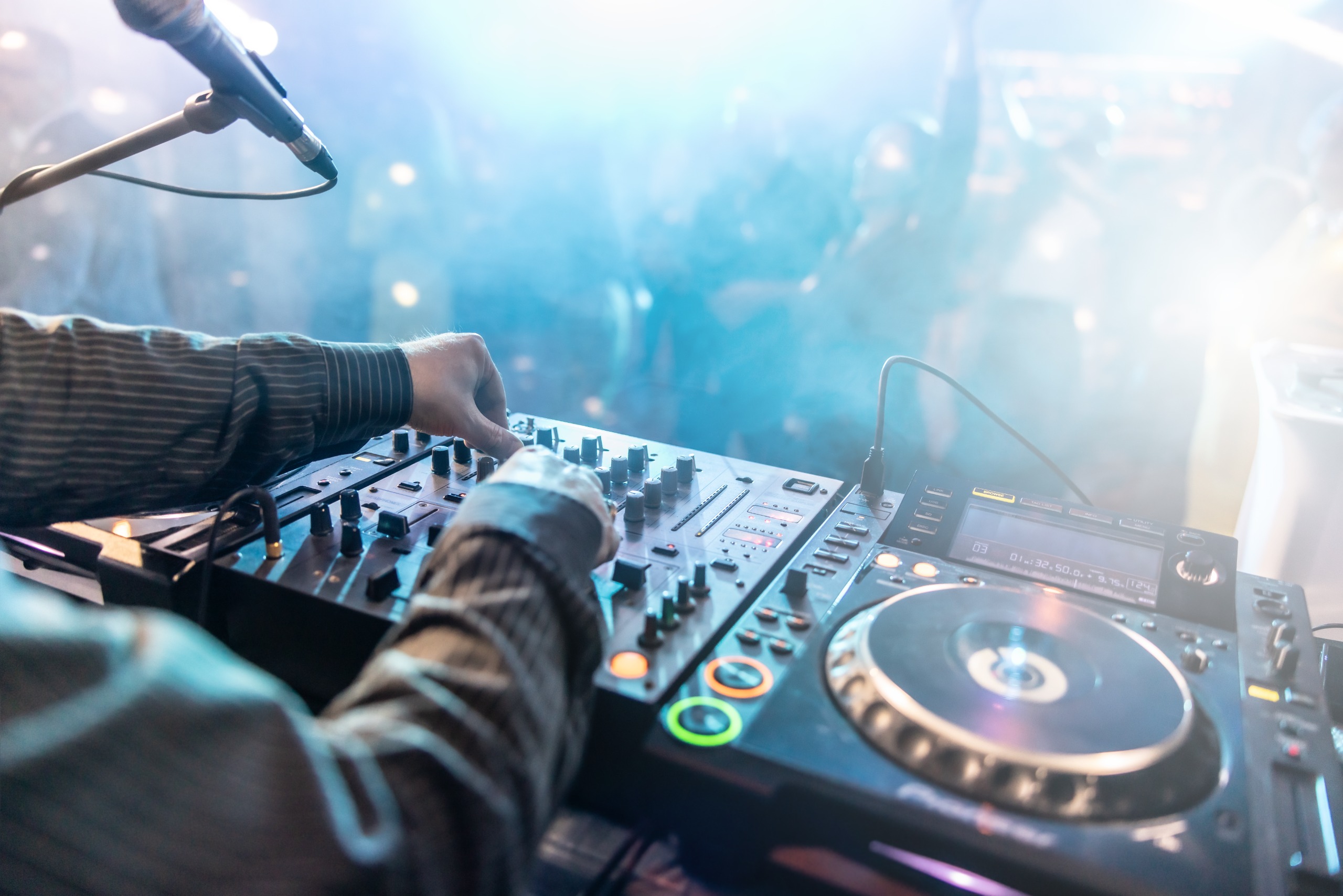 A DJ playing music in a nightclub as people dance under the neon lights.