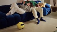 An image of Samsung's upcoming yellow Ballie AI robot sitting on the floor by a sofa.
