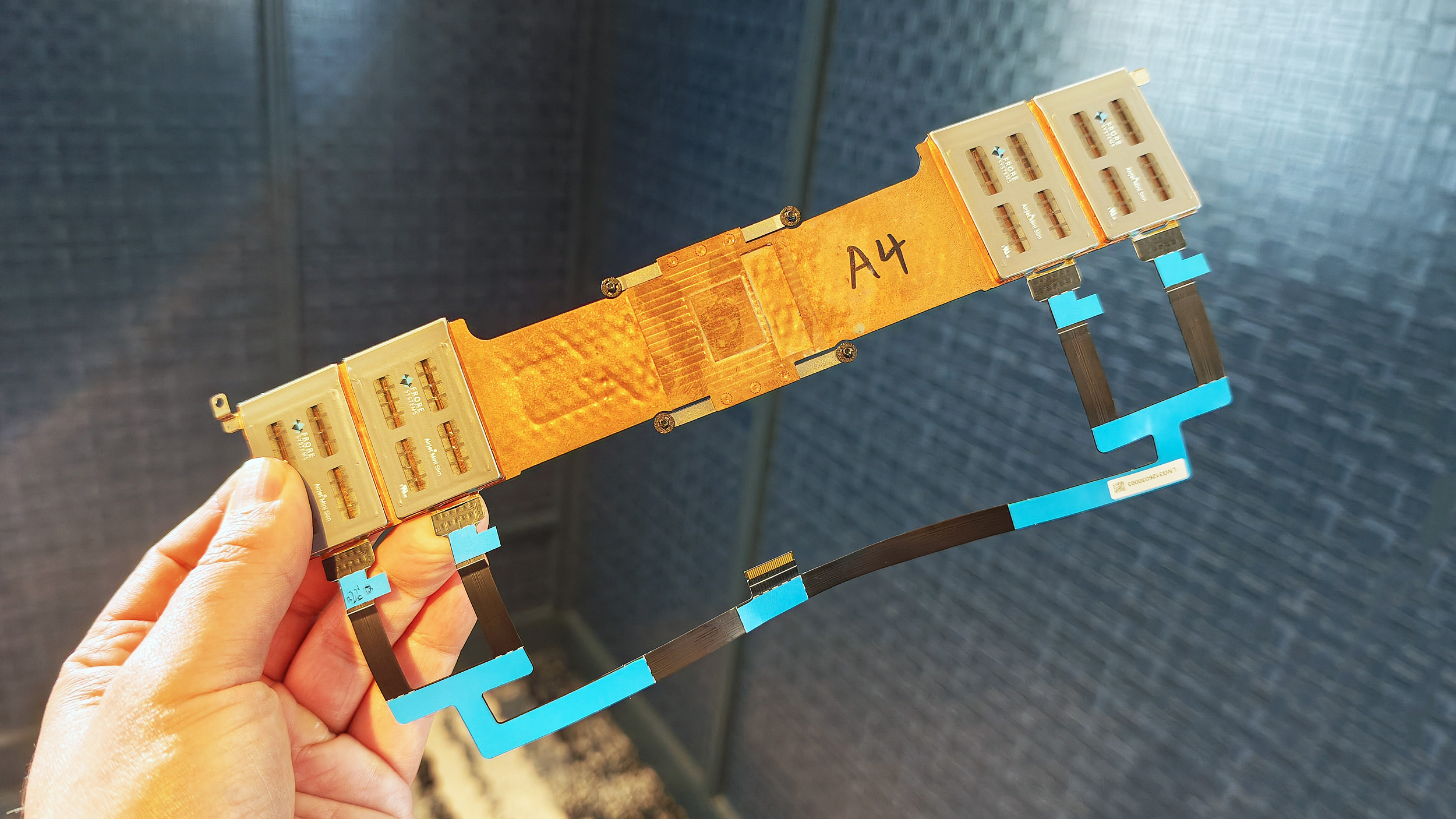 Hand holding a custom Frore AirJet solid-state cooling strip assembly with copper heat sinks and ribbon cables.