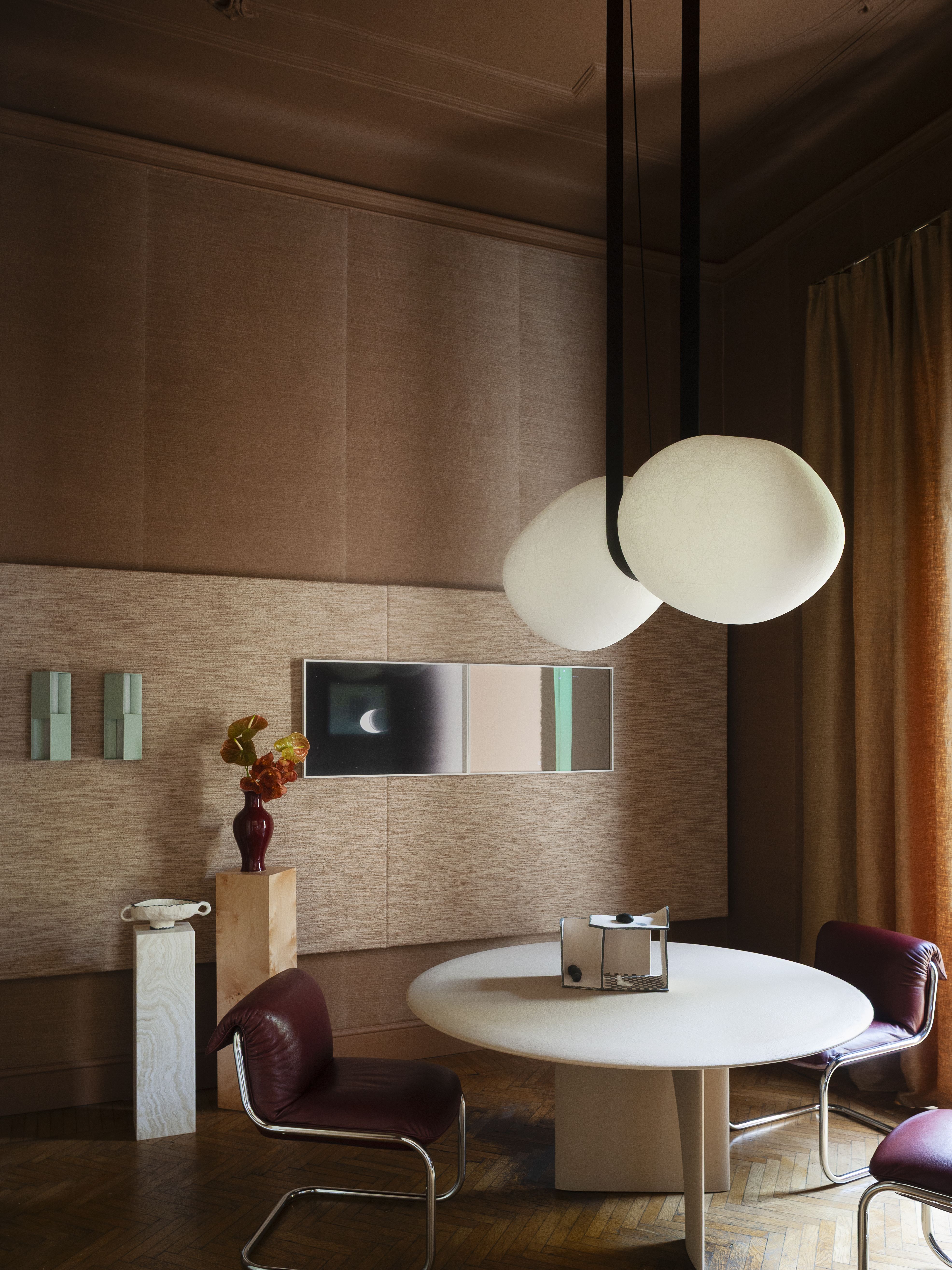 a dining room with brown paneled walls, a dining table, large ceiling lamps and mint wall decor