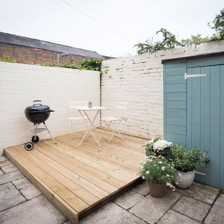 courtyard with white brick wall and barbecue and teal door and table and chair and pots
