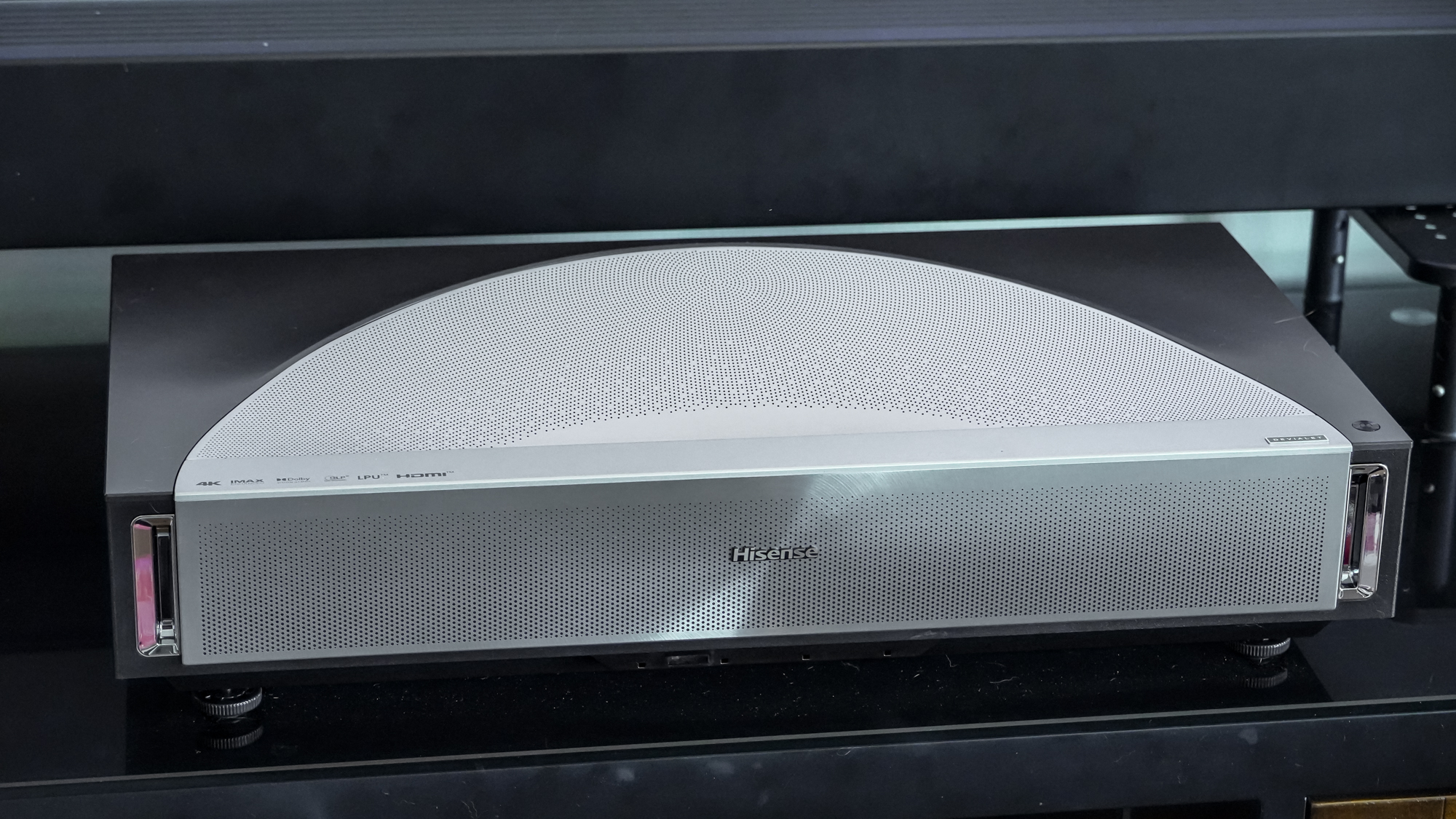 A Hisense PX4 Pro projector on a home media center shelf