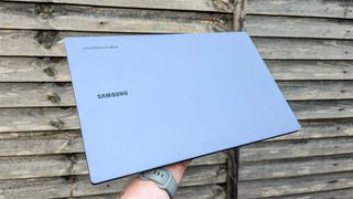 Samsung Galaxy Chromebook Plus closed held in hand in front of wooden fence