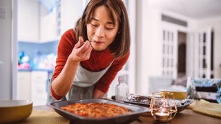 Young Asian woman tasting a dish of pasta she prepared while serving food on the table at home.