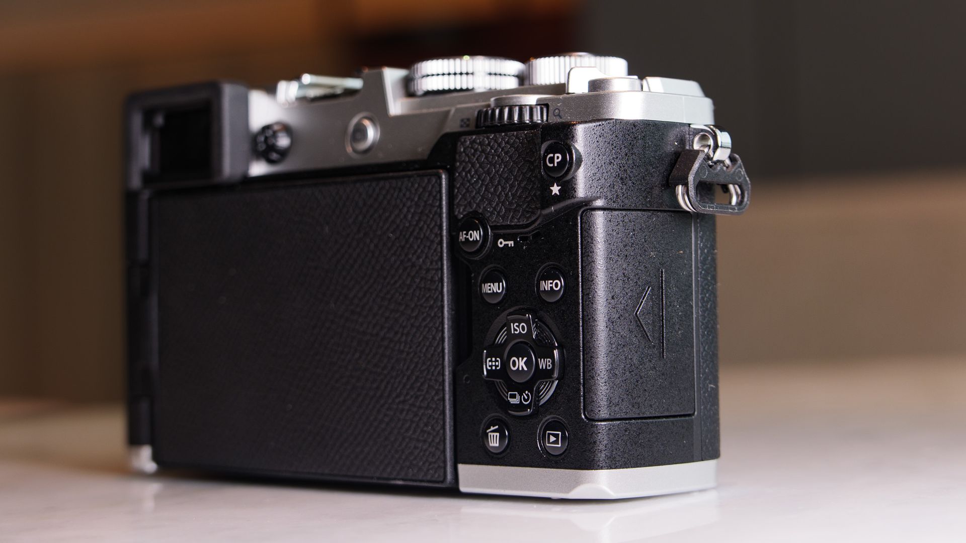 Close up of the OM System PEN mirrorless camera's memory card door, in a modern room with lantern in the background