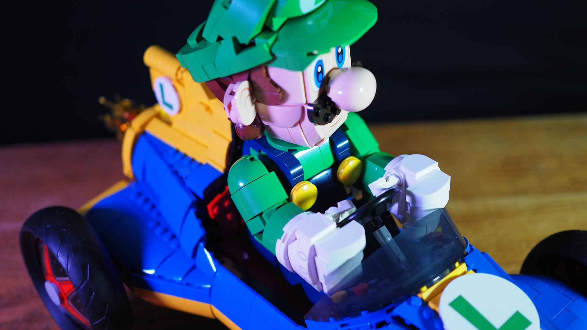 Lego Luigi looking to one side in the Mach 8 kart, on a wooden surface