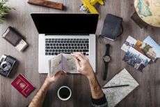 Man looking through his passport drinking coffee in front of an open laptop