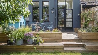 A raised deck area in front of a modern kitchen extension with raised beds and a garden bistro set