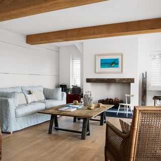 white living room with exposed wooden beams large fireplace patterned sofa and other chairs arranged around large wooden coffee table
