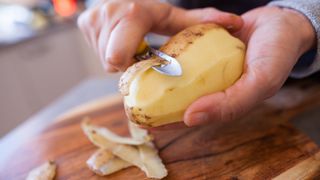 person peeling a potato on a wooden chopping board