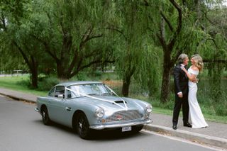 A couple on their wedding day beside a decorated classic car
