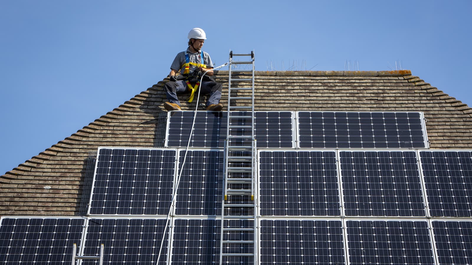 A maintenance person uses a ladder and harnesses to install equipment around a Solar panel
