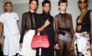 Models wear white skirt and top, black see through tops and red bag