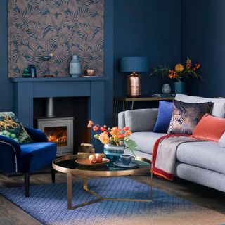 A deep blue living room with rich metallic coffee table, log burner and grey sofa