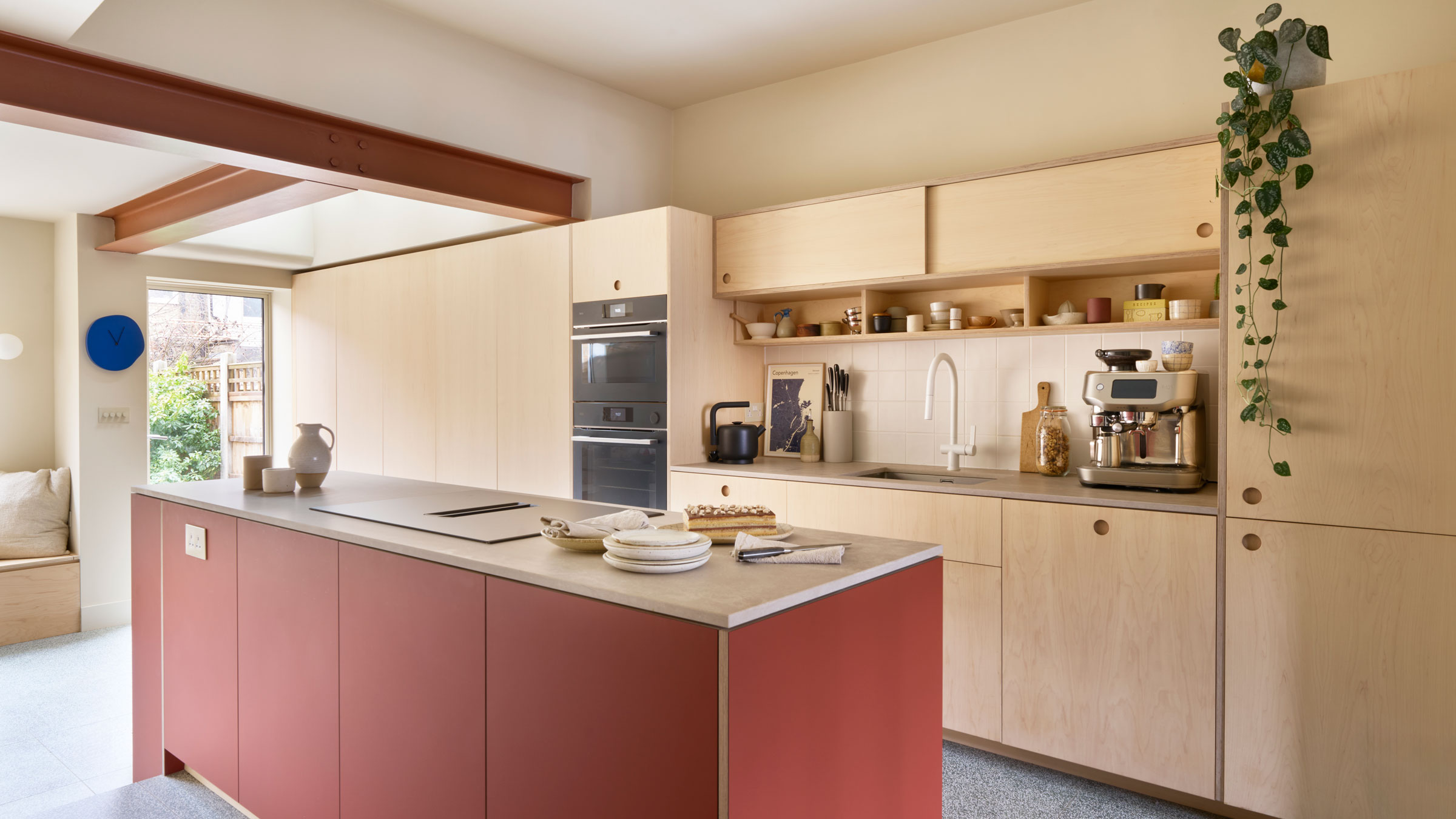 Plywood kitchen with a terracotta kitchen island and a trailing houseplant on top of the cabinet.