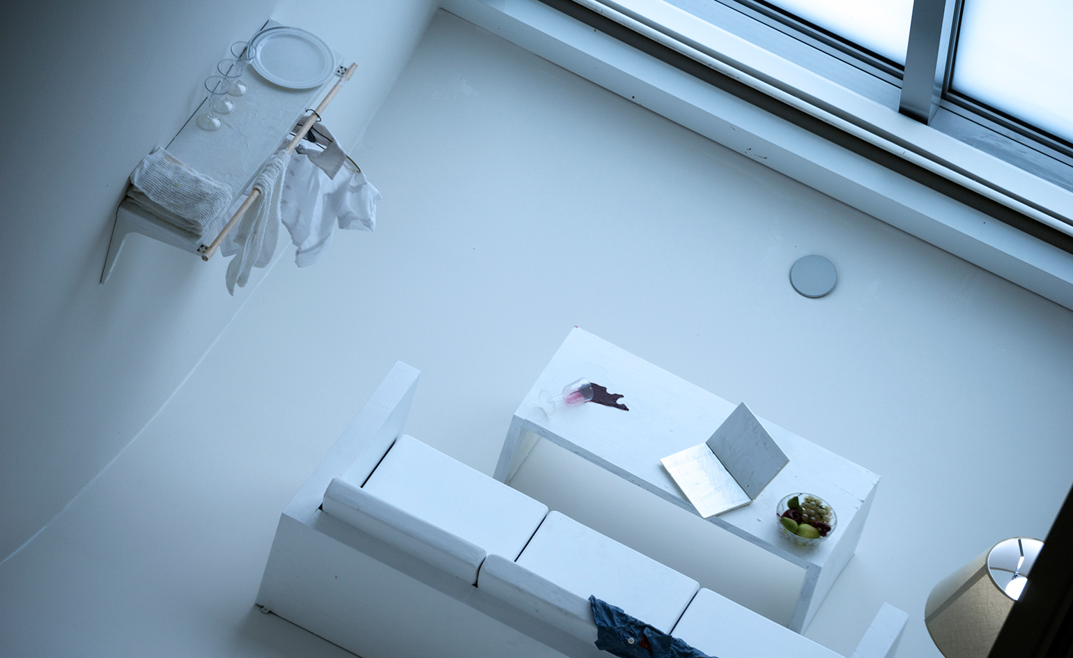 An all white room with white furniture and accessories and red wine spilled on the table