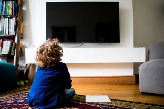 A child sat on the floor looking up a a blank TV screen