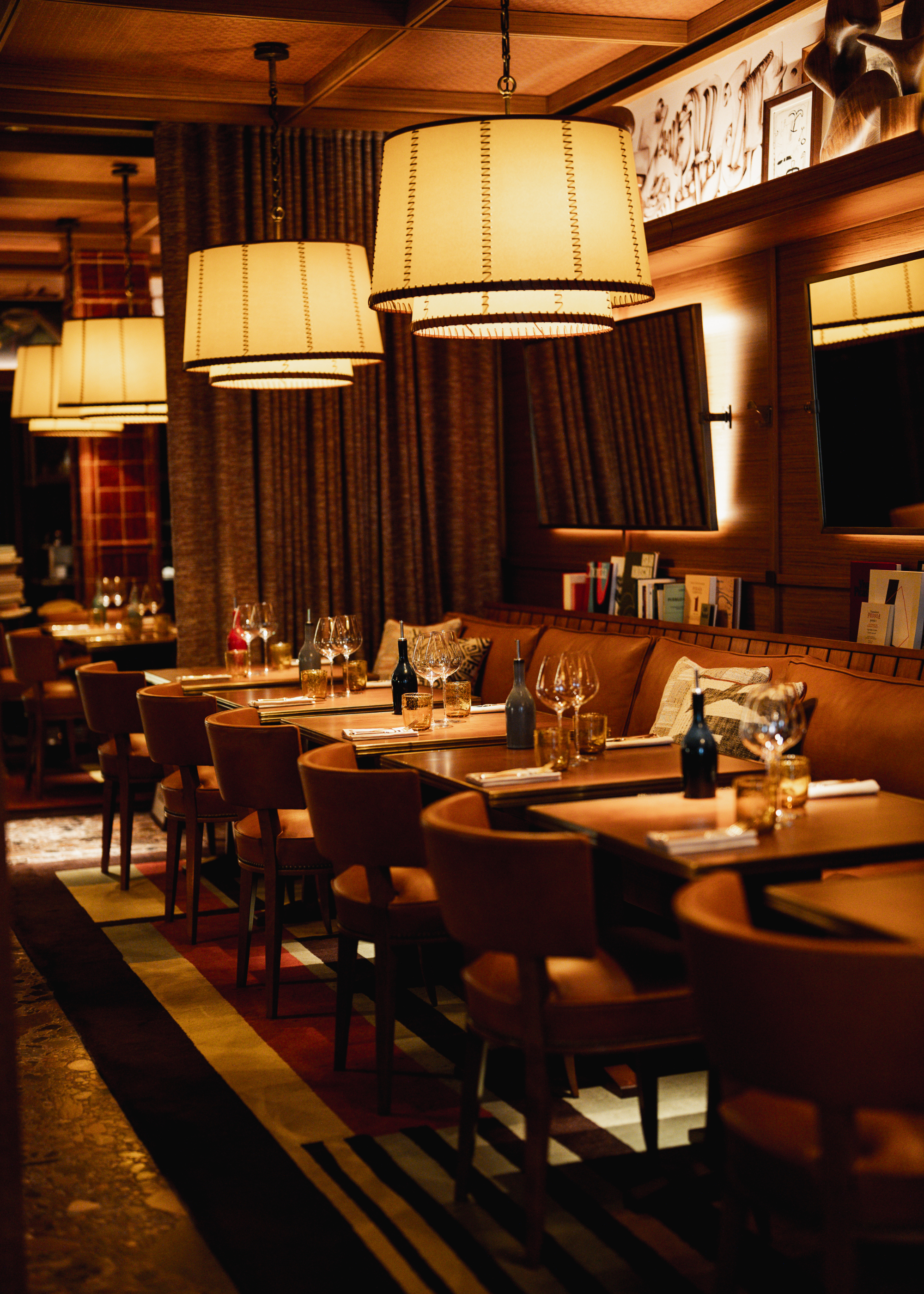 A hotel restaurant with warm lighting, curved dining chairs, and a wall-side couch with books and art in cabinets