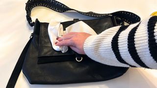 A hand dusting the outside of a leather bag with a lint-free cloth