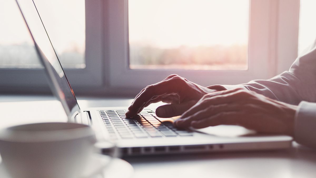 Close up photo of a person&amp;#039;s hands typing on laptop in a brightly-lit office