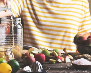 A woman wearing yellow and white striped t-shirt preparing a homemade apple cider vinegar solution using fresh apples and coarse sea salt