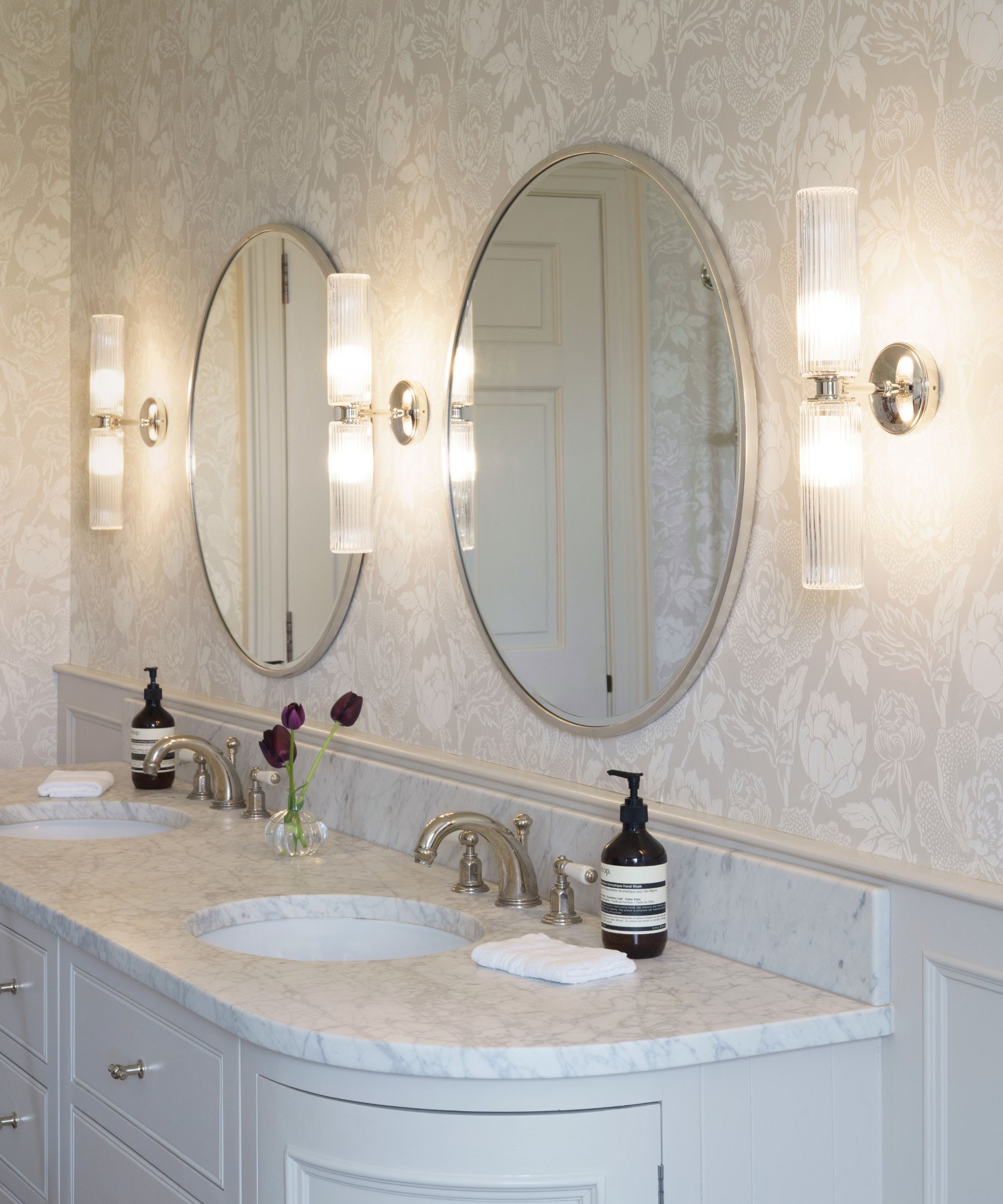 A his and her bathroom vanity with sinks and two oval mirrors above each sink with retro fluted glass wall lights either side of the mirrors