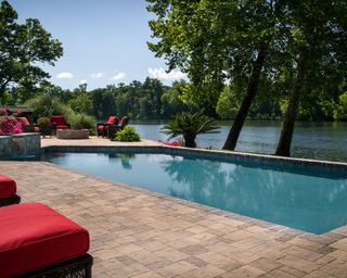 A large pool area with red sun loungers overlooking a river